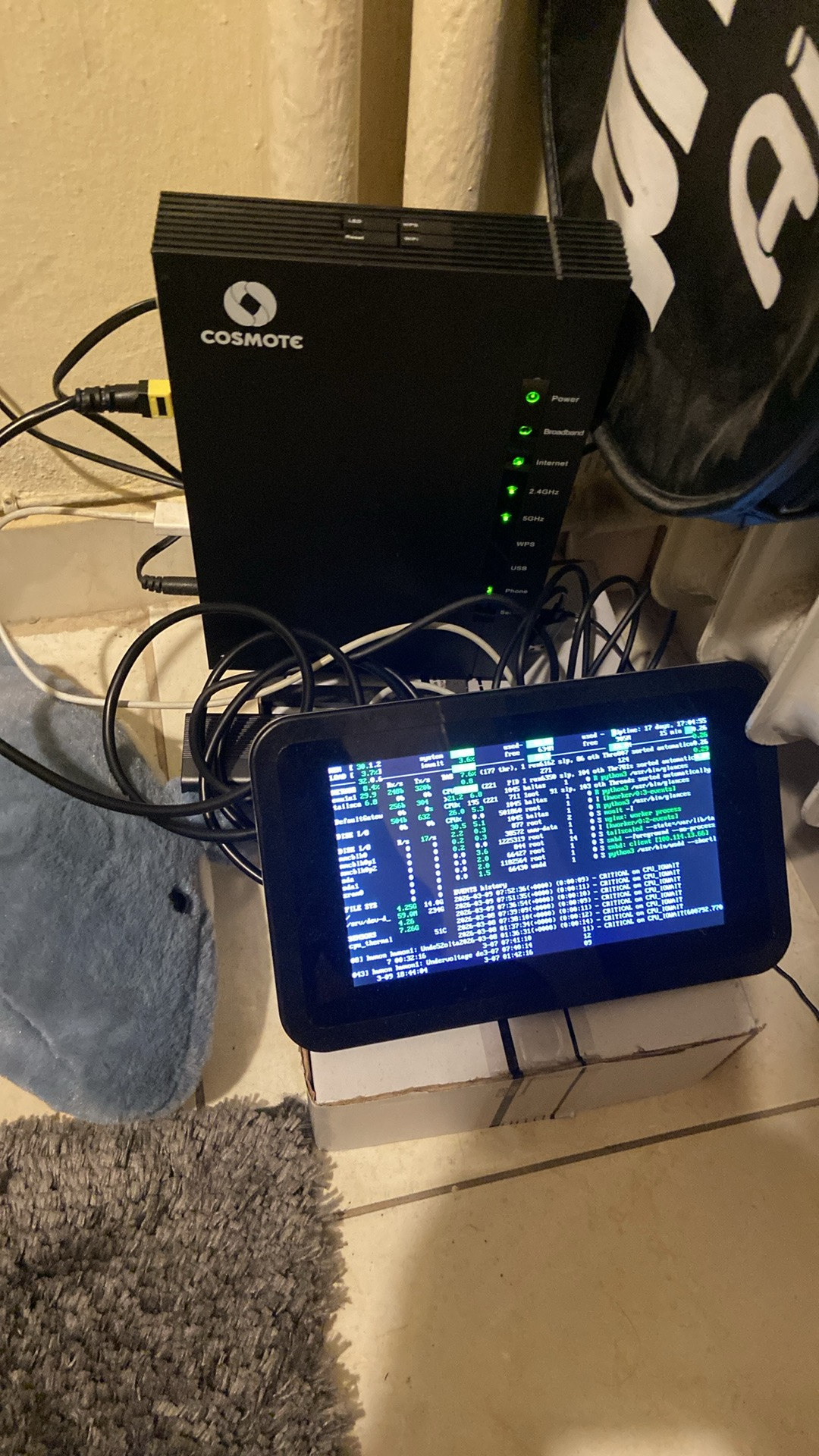 Cosmote router with a small Glances monitoring display propped up in front of it, cables running to the Raspberry Pi